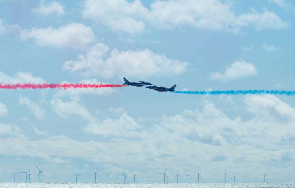 two airplanes flying in the sky with colored smoke coming out of them