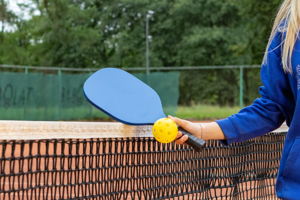 a woman holding a ping pong paddle over a tennis net
