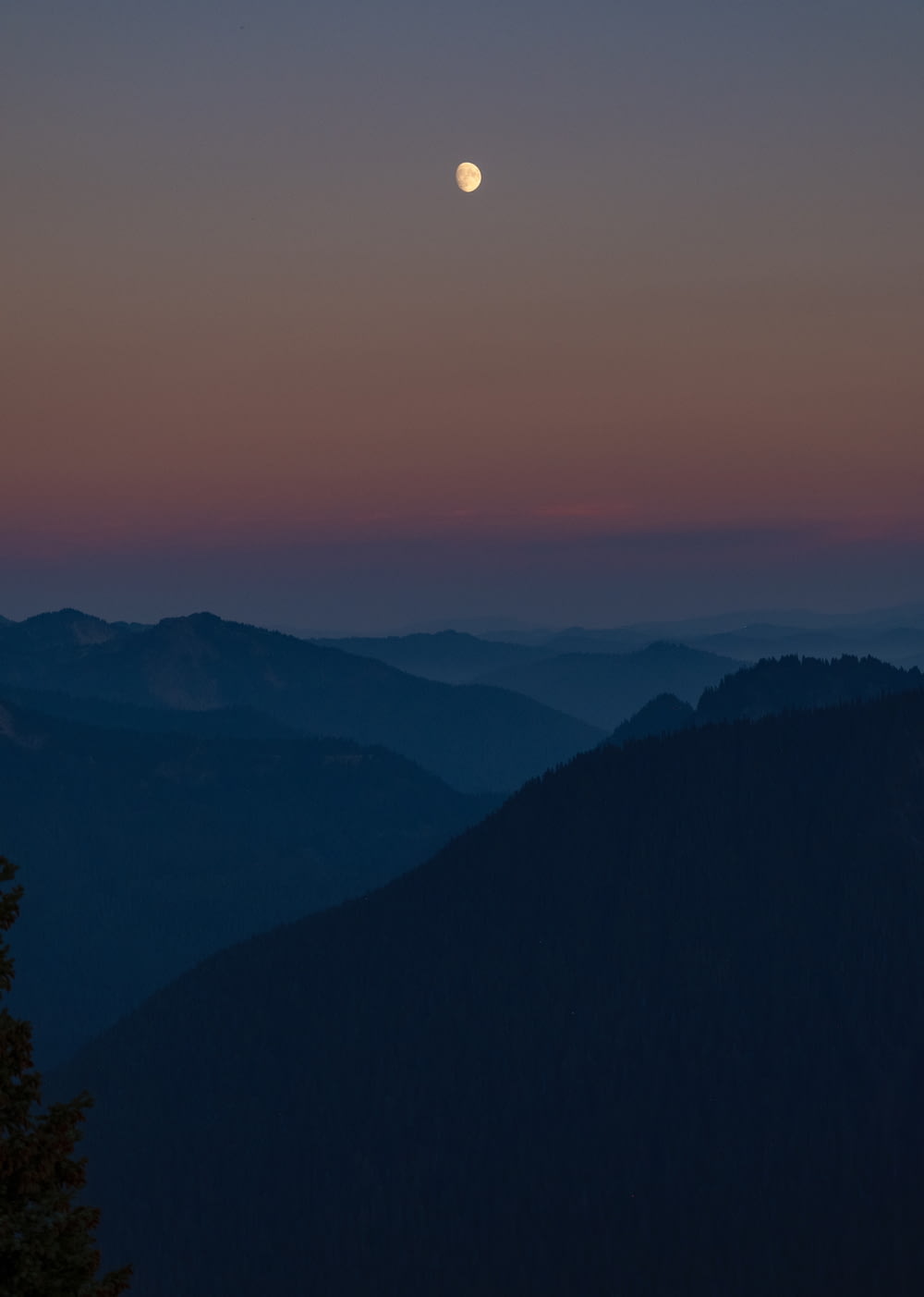 a full moon is seen over a mountain range