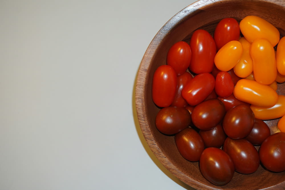 a wooden bowl filled with lots of different colored tomatoes