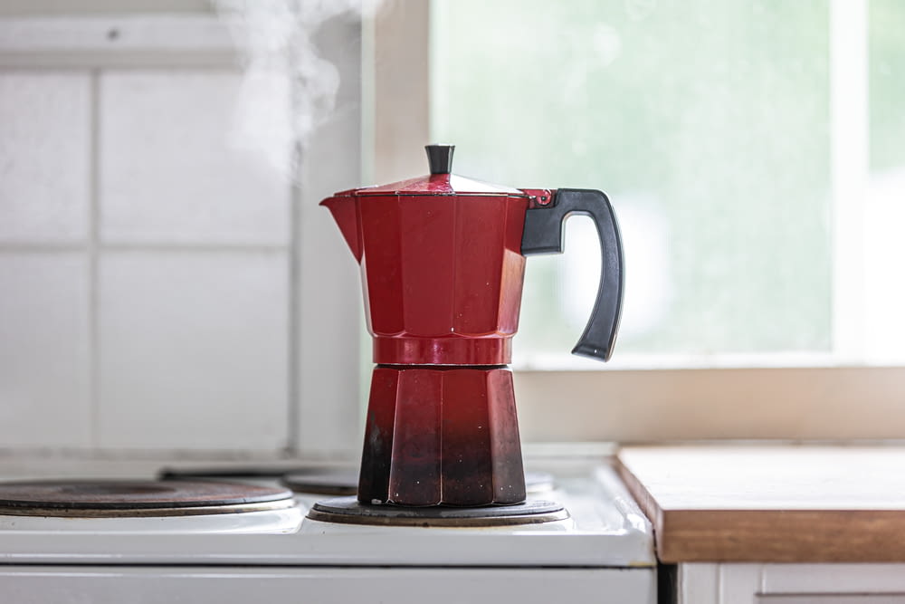 a red coffee pot sitting on top of a stove