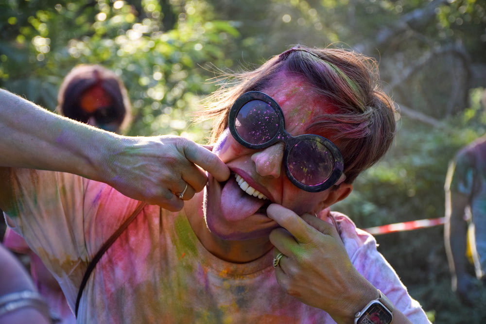 a woman is covered in colored powder and holding a pair of goggles to her