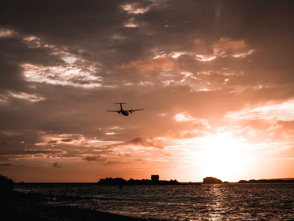 a plane flying over a body of water at sunset