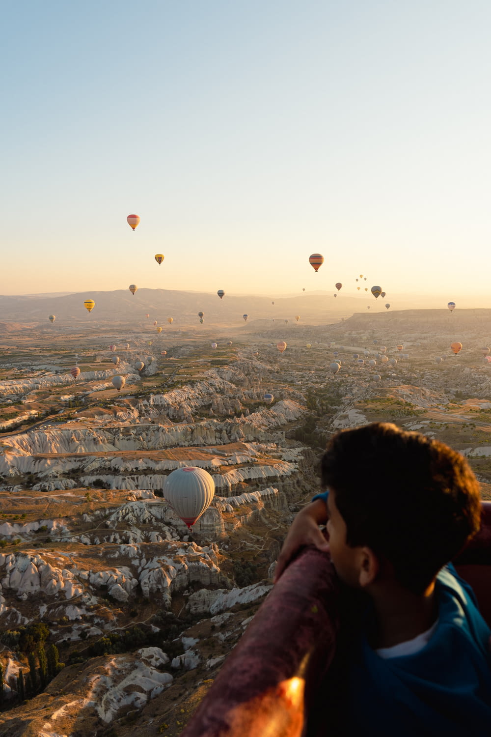 a man looking out over a valley with hot air balloons in the sky