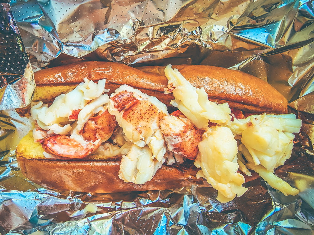 a hot dog with shrimp and potatoes on a piece of tin foil