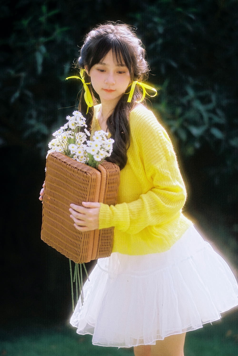 a girl in a yellow sweater holding a basket of flowers