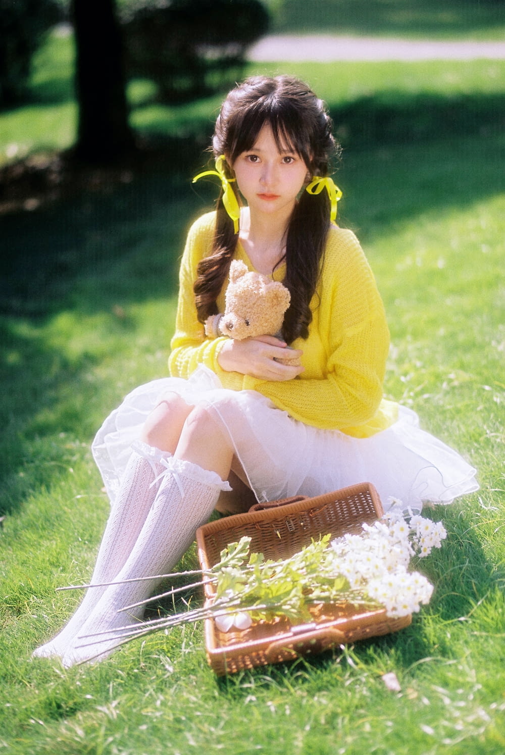 a woman sitting in the grass holding a teddy bear