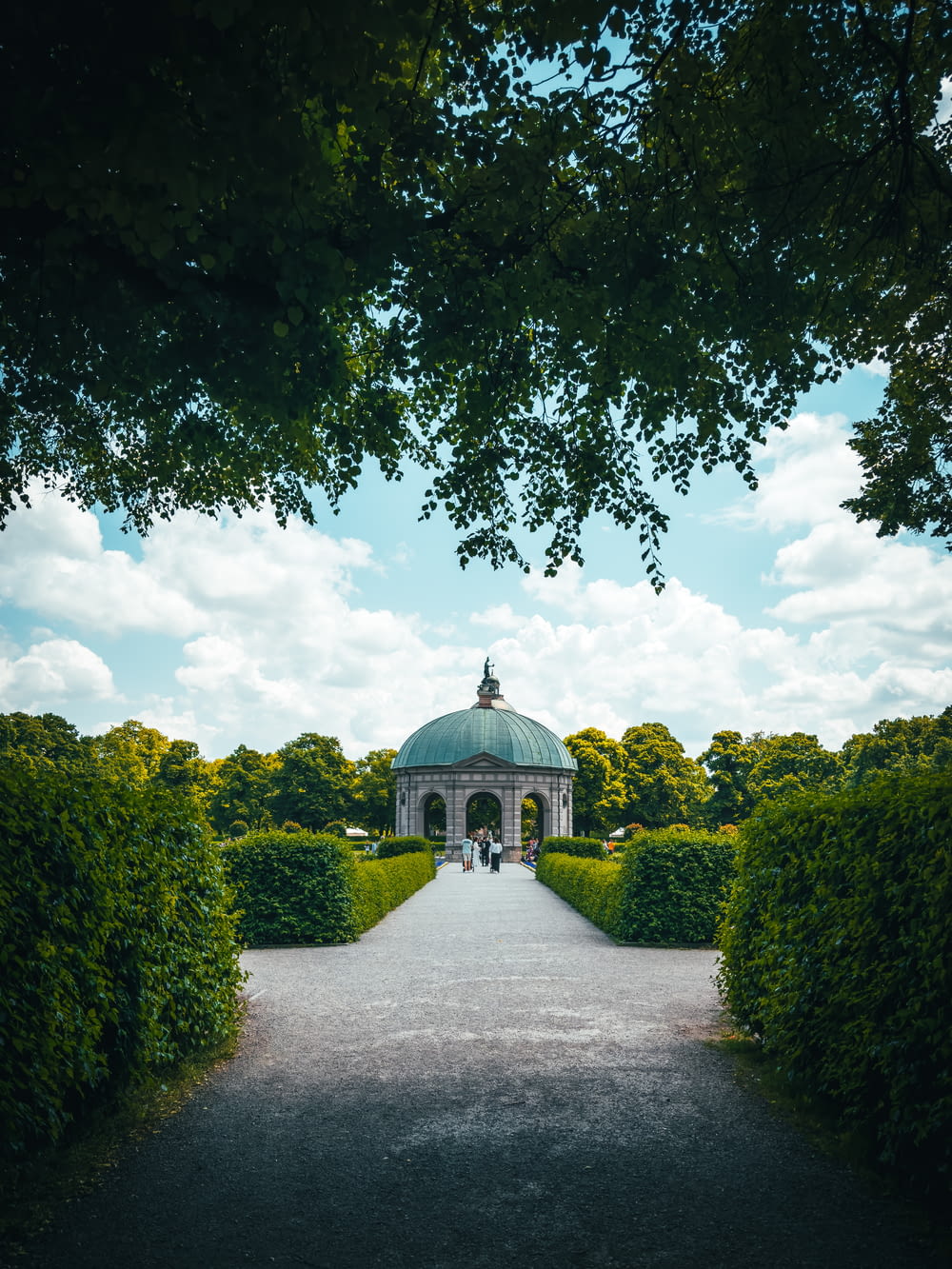 a gazebo surrounded by hedges and trees on a sunny day