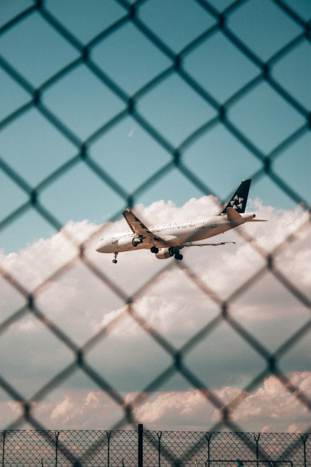 a plane is flying in the sky behind a chain link fence