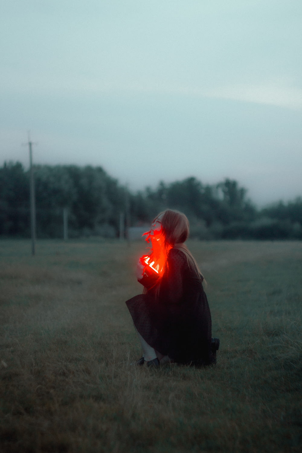 a woman kneeling down in a field with a red light on her face