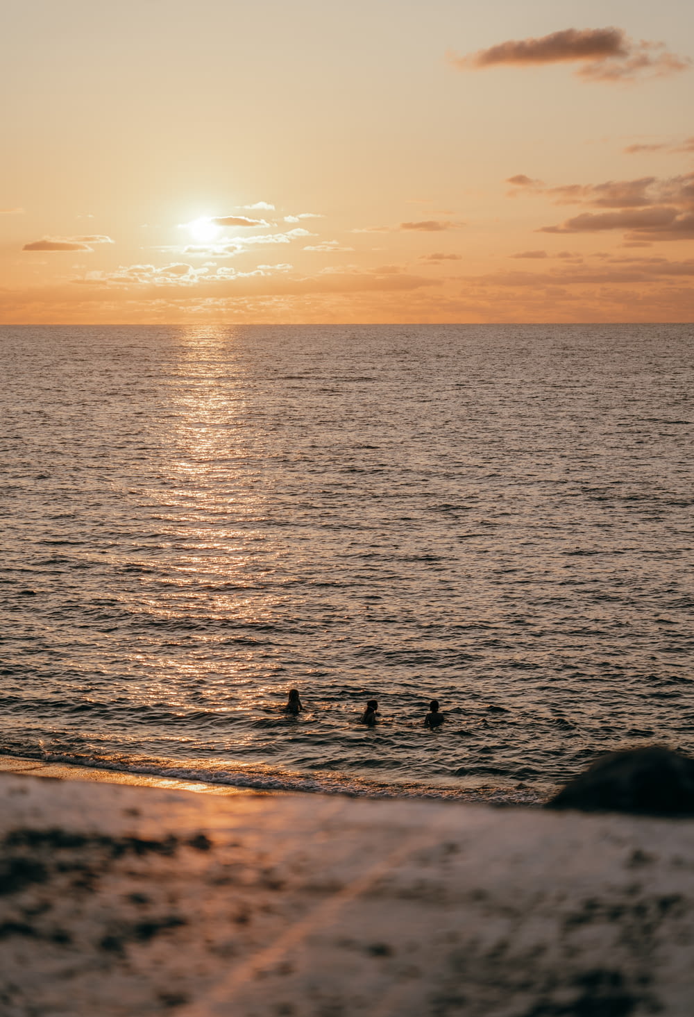 a couple of people swimming in the ocean at sunset