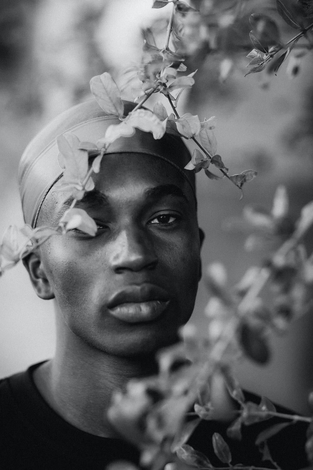a black and white photo of a young man with flowers on his head