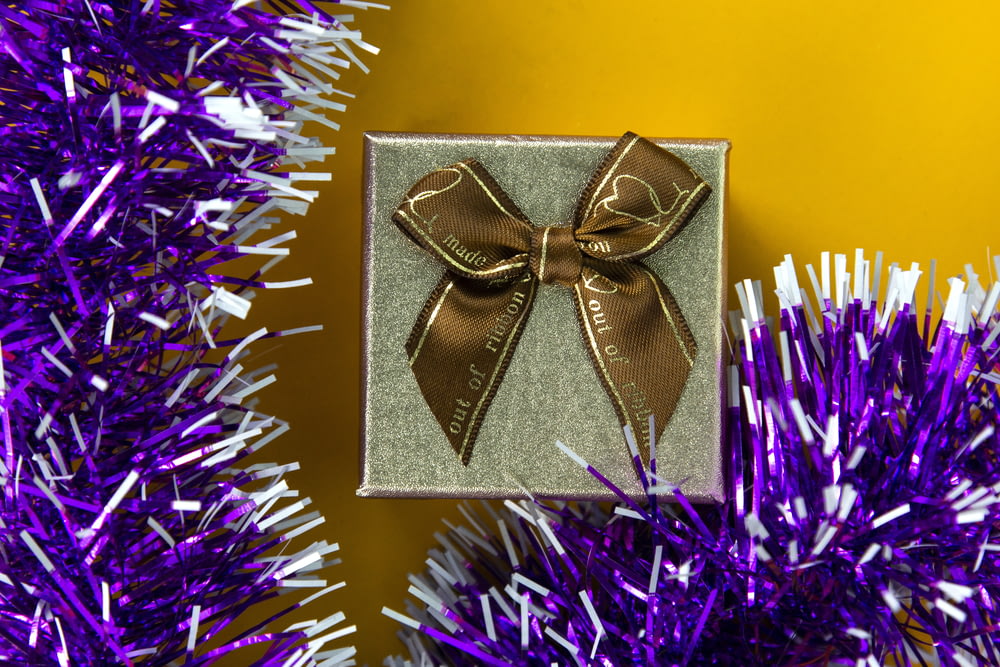 a gift wrapped in brown ribbon sitting on top of a purple christmas tree