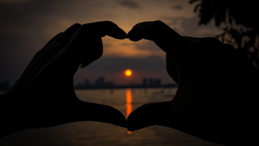two hands making a heart shape with the sun setting in the background