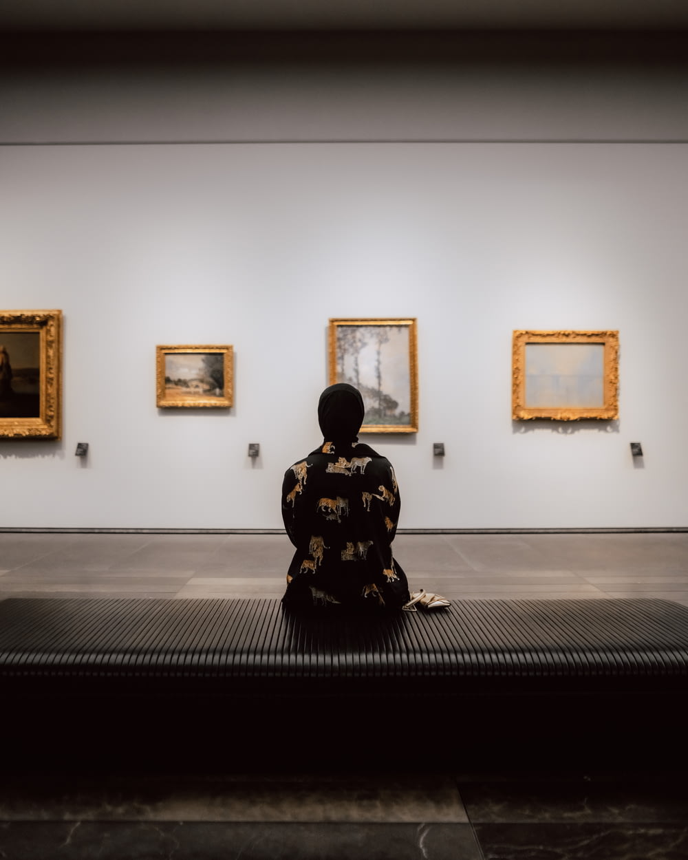 a person sitting on a bench in front of paintings