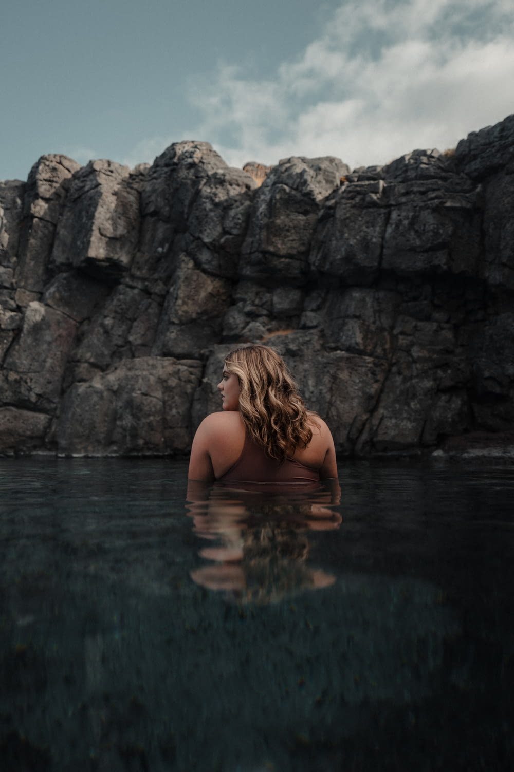 a woman in a body of water with rocks in the background