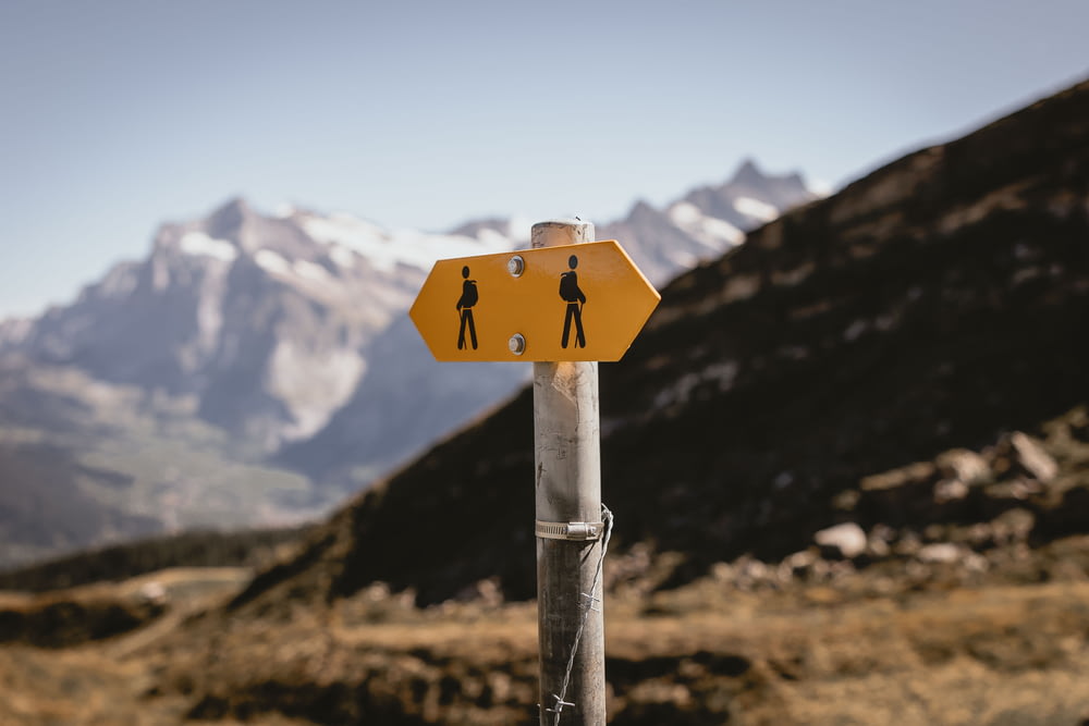 a yellow street sign on a pole with mountains in the background