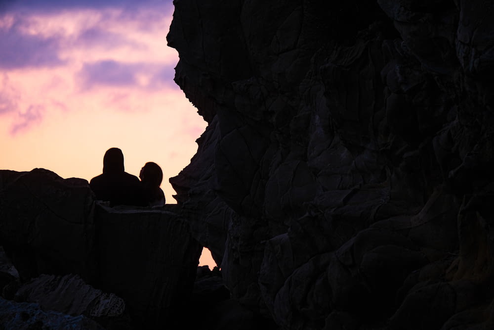 a couple of people sitting on top of a rocky cliff