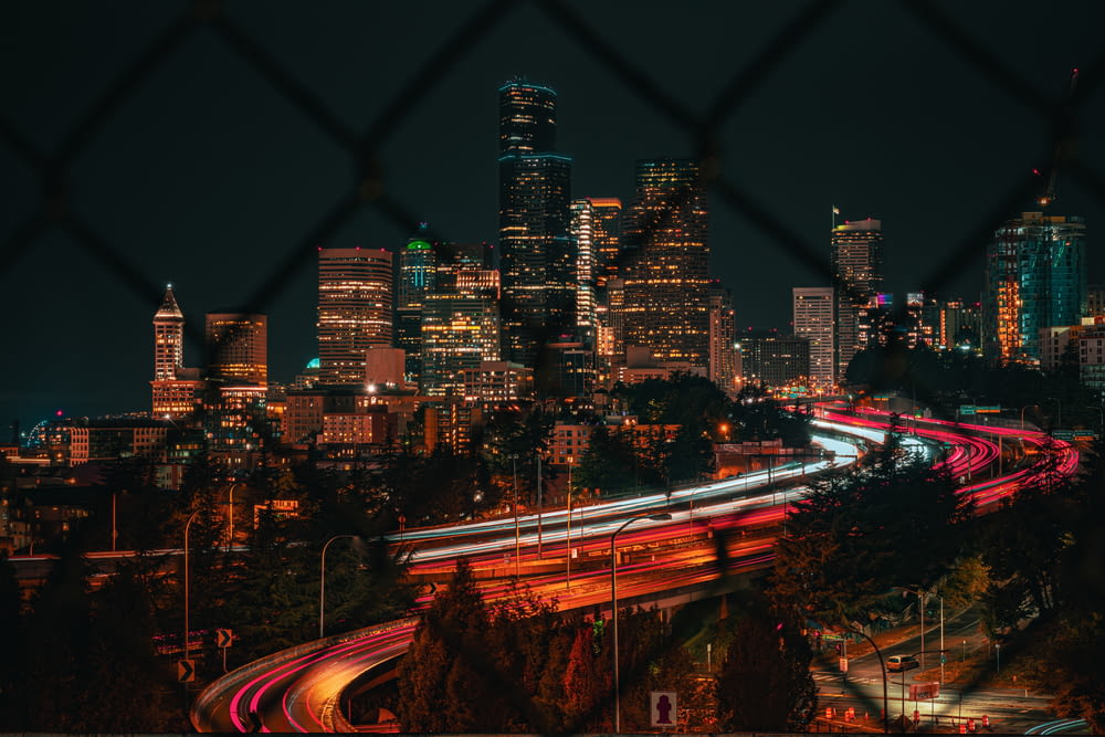 a view of a city at night through a chain link fence