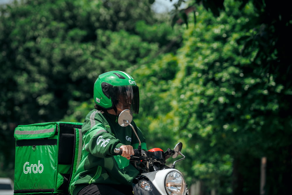 a person riding a motorcycle with a green bag on the back of it