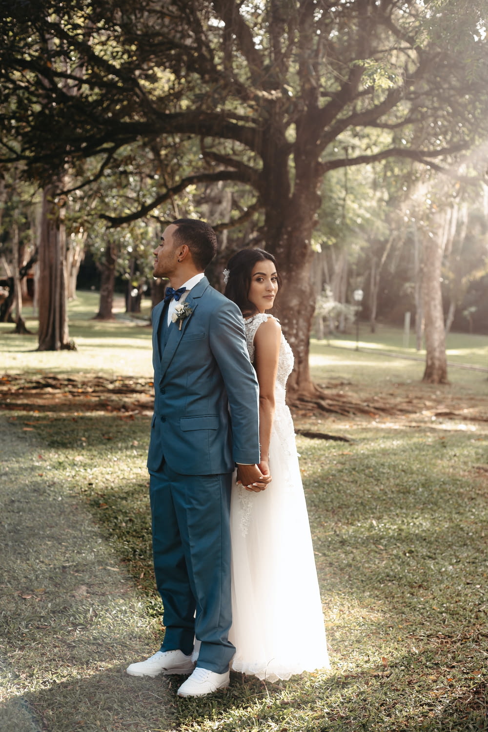 a bride and groom standing in the grass under a tree