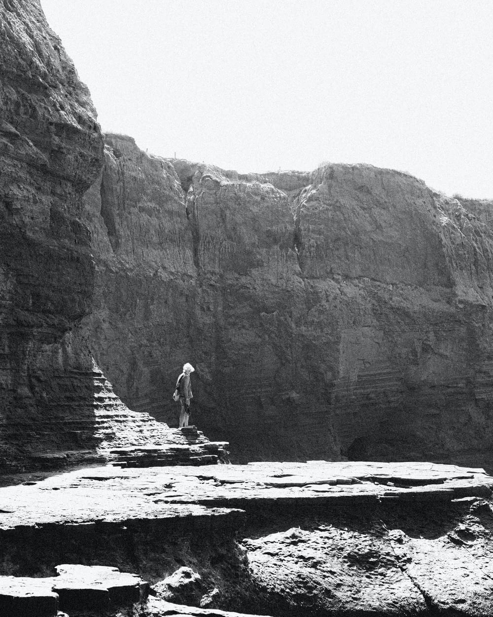 a black and white photo of a man standing on a cliff