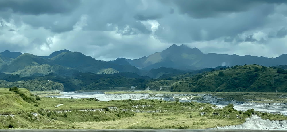 a scenic view of a river and mountains under a cloudy sky