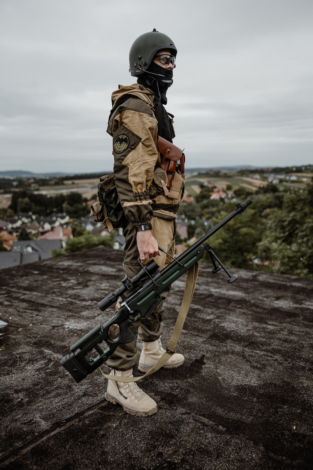 a man in camouflage holding a rifle on top of a roof