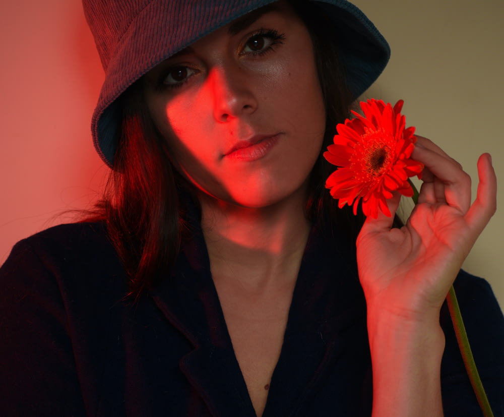 eine Frau mit Hut hält eine rote Blume