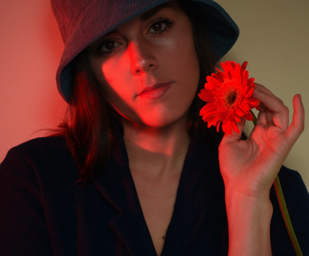 a woman in a hat holding a red flower