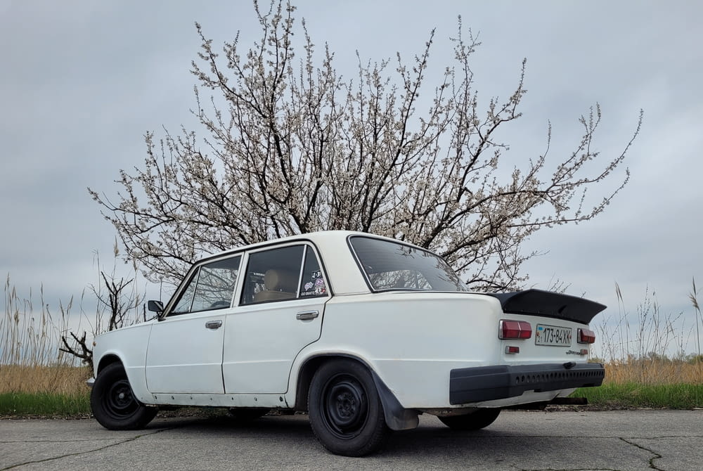 an old white car parked in front of a tree