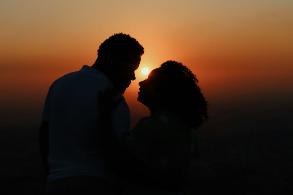 a man and a woman standing in front of a sunset