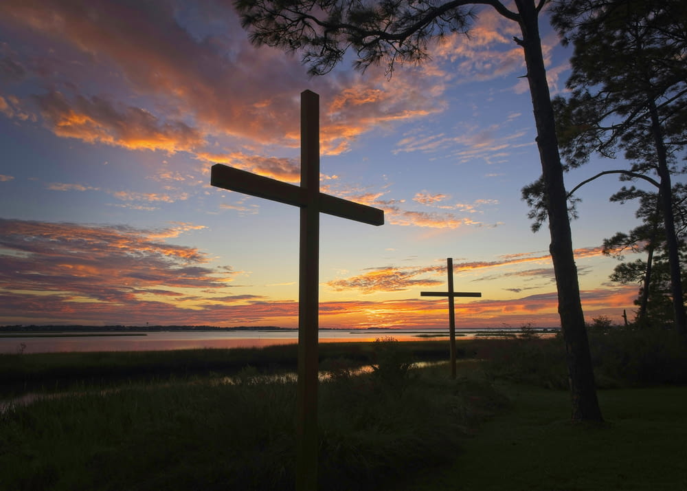 a cross is silhouetted against a sunset over a body of water