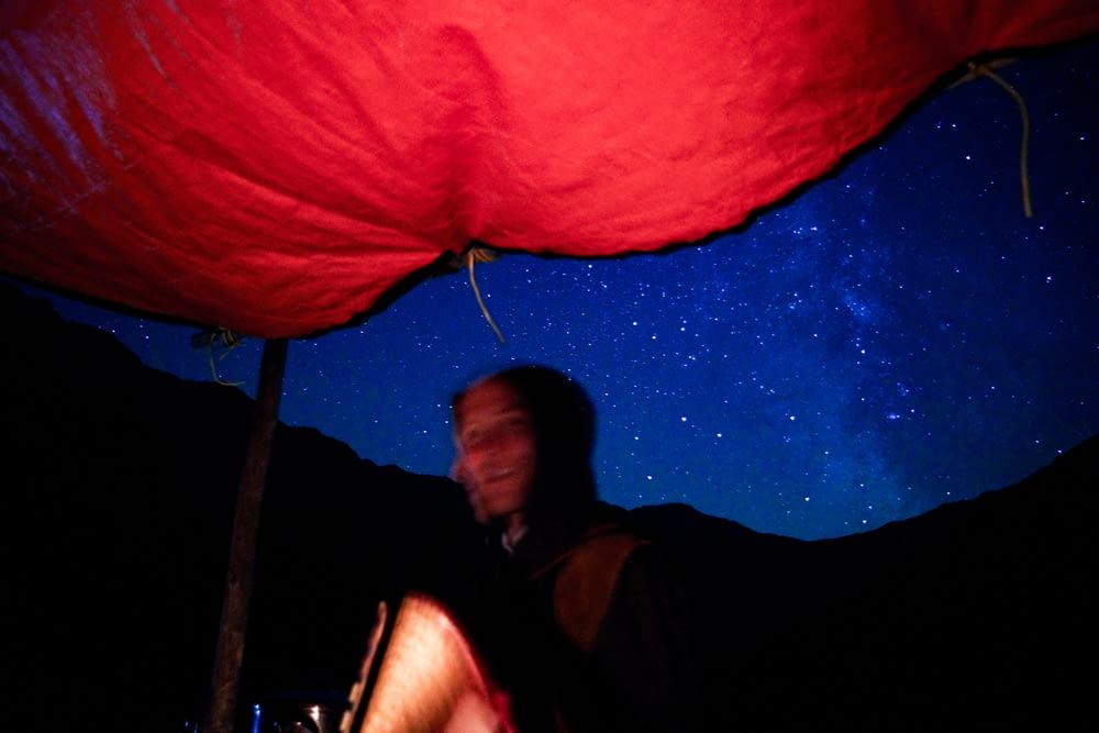 a man sitting under a red umbrella under a night sky