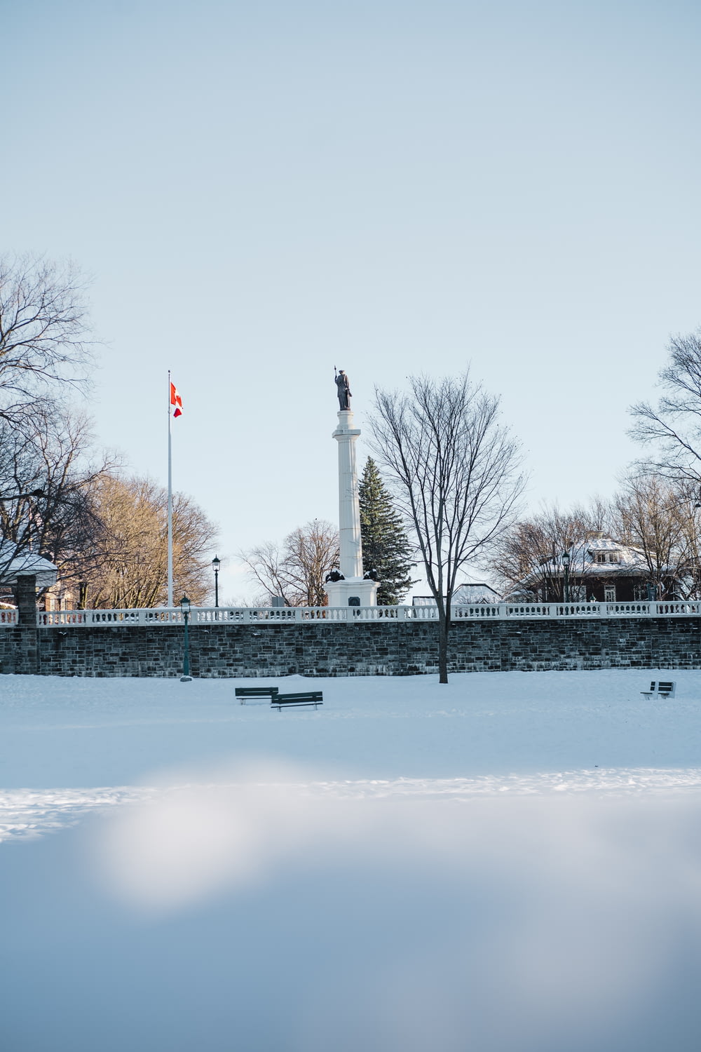 a snowy park with benches and a monument in the background