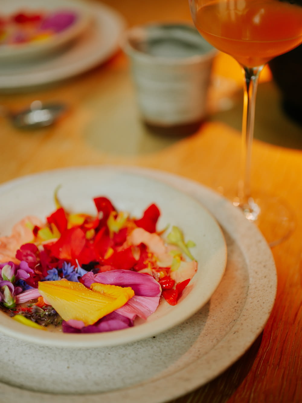 a white bowl filled with flowers next to a glass of wine