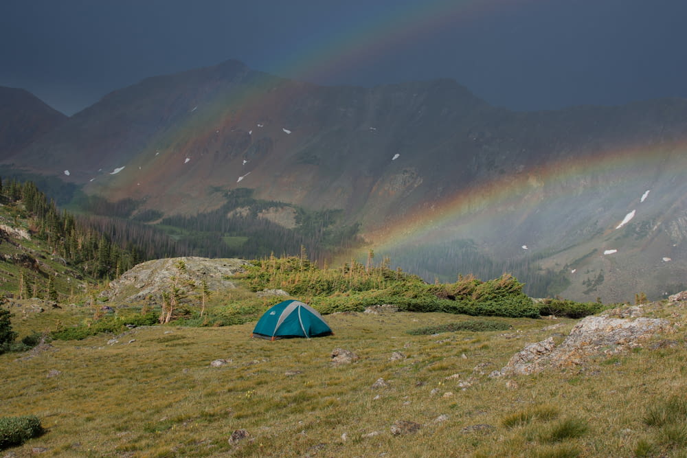 a tent in a field with a rainbow in the background
