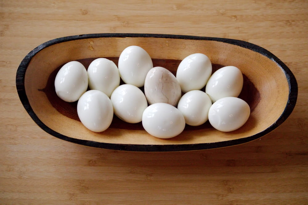 a wooden bowl filled with white eggs on top of a wooden table