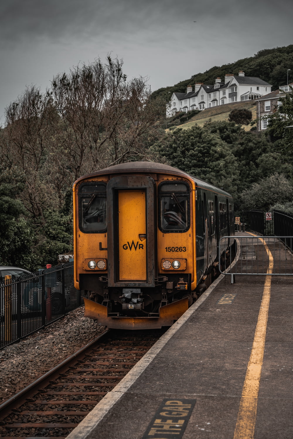 Ein gelber Zug, der auf Bahngleisen neben einem üppig grünen Hügel fährt