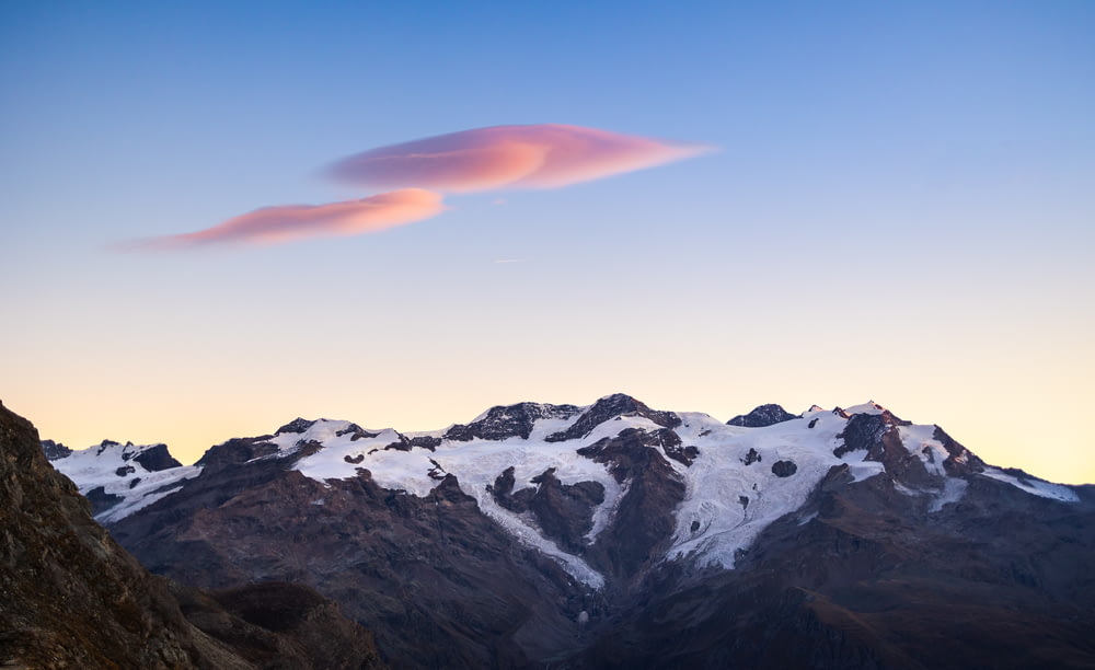 a pink cloud in the sky over a mountain range