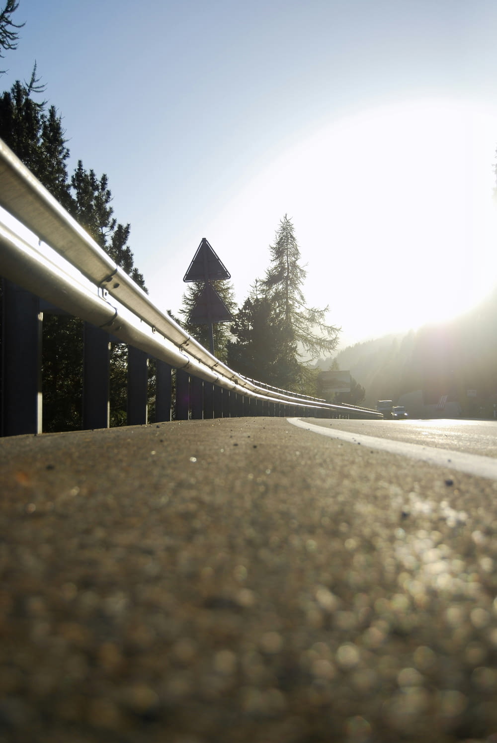 the sun is shining on a road with a metal railing