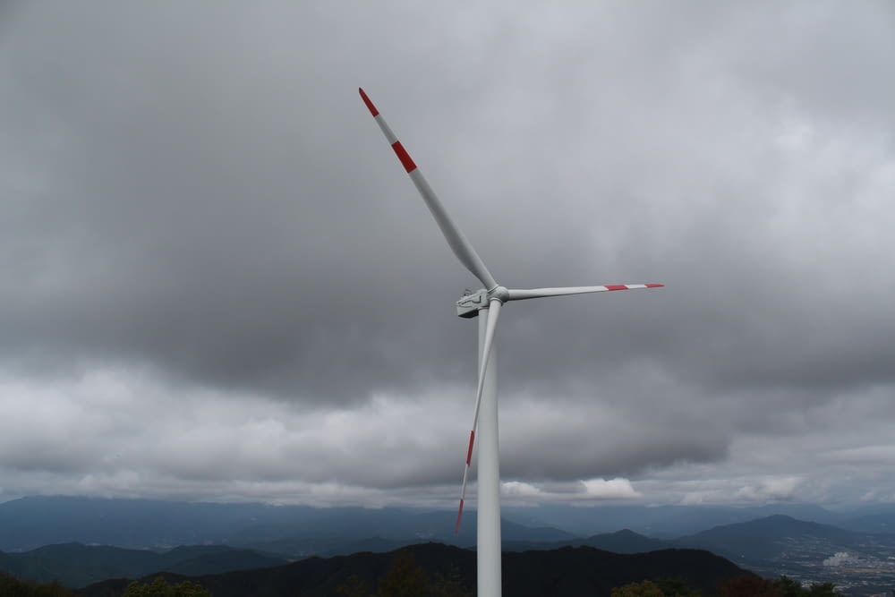 a wind turbine on a cloudy day with mountains in the background