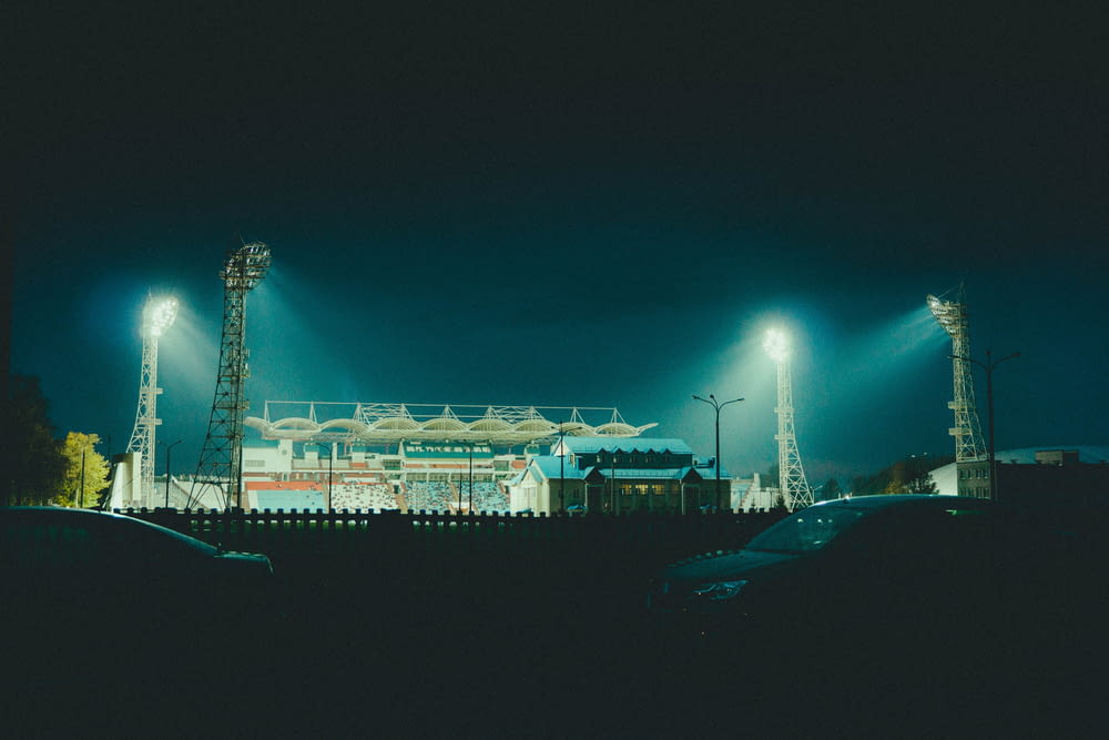 a stadium lit up at night with cars parked in front of it