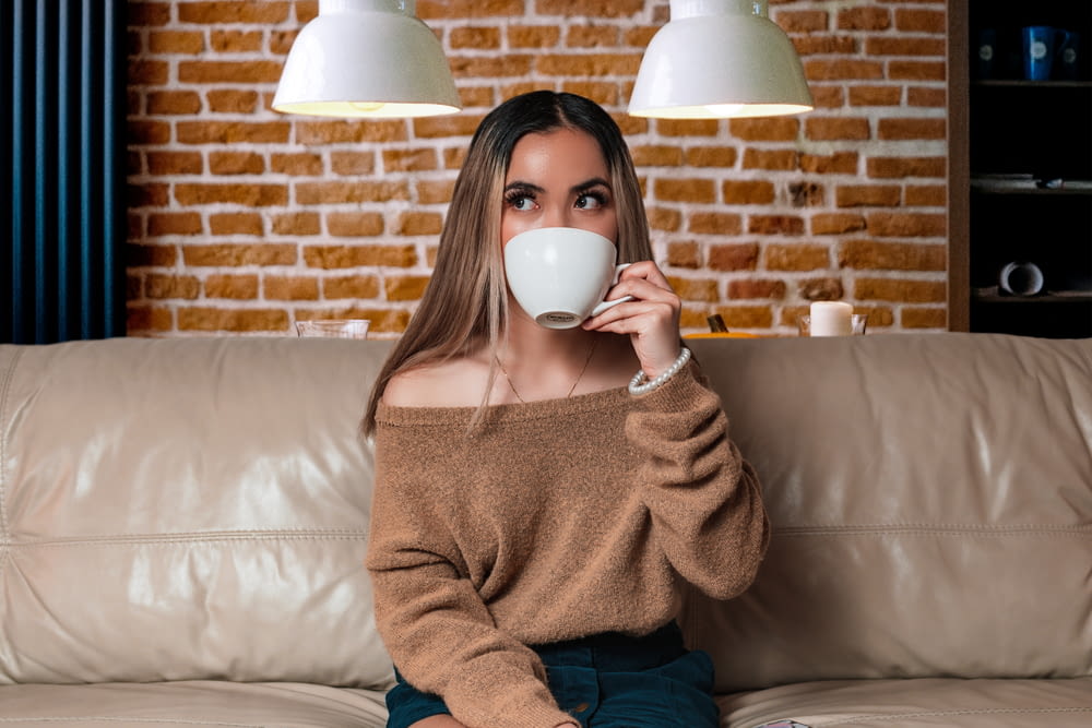 a woman sitting on a couch drinking a cup of coffee