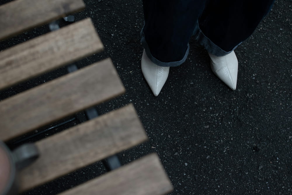 a person wearing white shoes standing next to a wooden bench