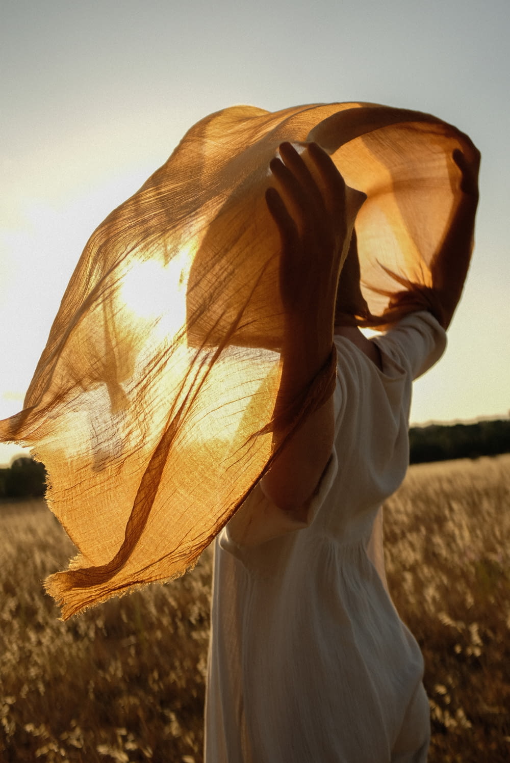 a woman standing in a field holding a yellow scarf over her head