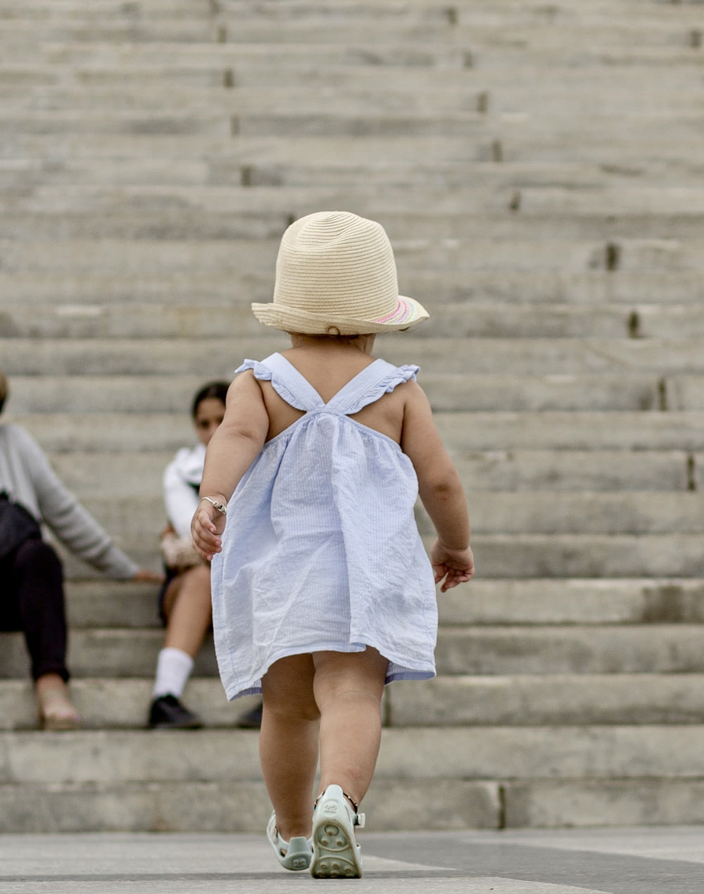 a little girl in a dress and hat walking down some steps