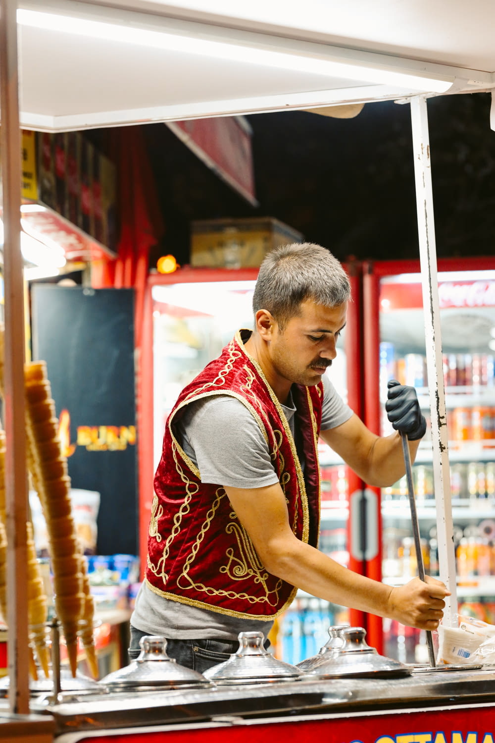 a man in a red vest standing at a food stand