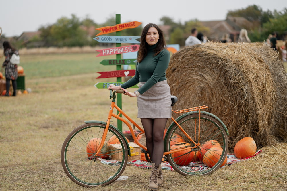 a woman standing next to a bike next to a hay bale