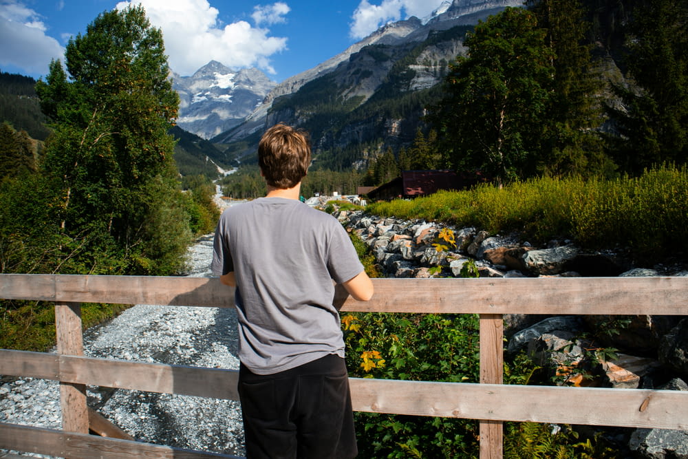 a boy standing on a bridge looking at a mountain stream